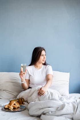 Junge brünette Frau sitzt wach im Bett mit roten herzförmigen Luftballons und Dekorationen, trinkt Champagner und isst Croissants. Valentines Day. Young brunette woman sitting awake in the bed with red heart shaped balloons and decorations drinking champagne eating croissants (License=RF) ,model released, Symbolfoto Copyright: xZoonar.com IlonaxShorokhovax 25401541 ,model released, Symbolfoto ,property released