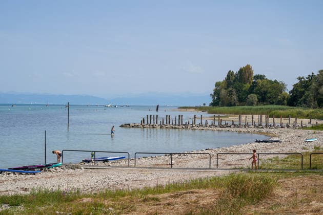 Schweiz, Bodensee: Niedriger Wasserstand legt breite Kies- und Uferflächen frei. Badegäste stehen im flachen Wasser, SUP-Boards liegen am Ufer; im Hintergrund Boote und Alpenpanorama. Symbolbild für Bodensee, Wasserstand, Niedrigwasser, Trockenheit, Hitze, Hitzewelle, Sommer, Klimawandel, Gewässer, Ufer, Kiesstrand, Baden, Abkühlung, Freizeit, Wassersport, Natur, Umwelt, Schweiz. *** Switzerland, Lake Constance: Low water levels expose wide stretches of gravel and shoreline; swimmers stand in shallow water, SUP boards lie on the shore in the background; boats and an Alpine panorama. Stock image representing Lake Constance, water level, low water, drought, heat, heat wave, summer, climate change, bodies of water, shore, gravel beach Copyright: xJOERANxSTEINSIEKx
