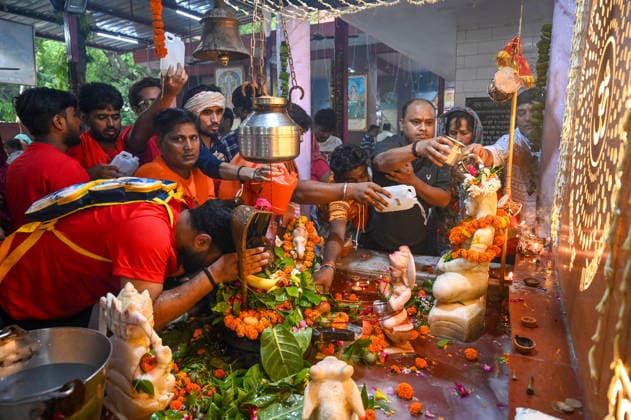 NOIDA, INDIA - AUGUST 11: Kanwariyas offering water on the Shivling with their families at the Kalariya Baba Temple in Sector 12 during Sawan Shivratri on August 11, 2026 in Noida, India. Shravan Shivratri is a sacred Hindu festival dedicated to Lord Shiva, observed on the Krishna Paksha Chaturdashi tithi of the holy month of Shravan. The festival commemorates Lord Shiva consuming the Halahala poison to save the universe during the churning of the cosmic ocean. The devotees bath the shivlinga with Gangajal, raw milk, honey, curd, ghee (Panchamrit) and other cooling liquids to help soothe his intense heat. (Photo by Sunil Ghosh Hindustan Times) Devotees Throng Shiva Temples On Occasion Of Shravan Shivratri Festival