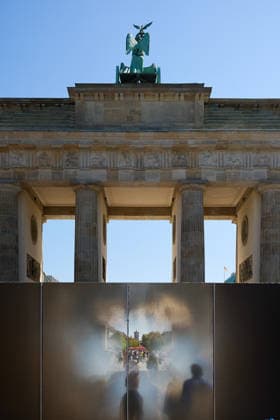 Ein temporaerer Gedenkort am Brandenburger Tor soll zum 65. Jahrestag des Mauerbaus an die deutsche Teilung erinnern (Foto vom 12.08.2026, im Bild: Menschen hinter der Installation). Die rund drei Meter hohe und 30 Meter lange Installation des Kuenstlers Hubertus Hamm auf dem Platz des 18. Maerz soll an die einstigen Grenzanlagen erinnern. Je nach Perspektive wirkt die Wand aus Aluminium lichtundurchlaessig oder transparent. (Siehe epd-Meldung vom 12.08.2026) EDITORIAL USE ONLY *** A temporary memorial site at the Brandenburg Gate is intended to commemorate the division of Germany on the 65th anniversary of the construction of the Berlin Wall. Photo taken on August 12, 2026, showing people behind the installation. The installation by artist Copyright: epd-bild ChristianxDitsch D26D0812MauerbauInstallation112504