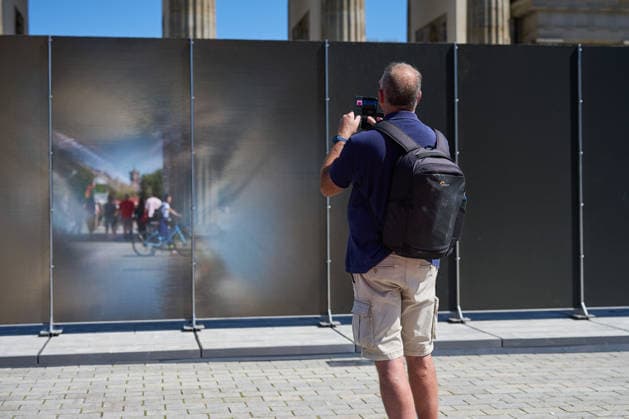 Ein temporaerer Gedenkort am Brandenburger Tor soll zum 65. Jahrestag des Mauerbaus an die deutsche Teilung erinnern (Foto vom 12.08.2026, im Bild: Menschen vor und hinter der Installation). Die rund drei Meter hohe und 30 Meter lange Installation des Kuenstlers Hubertus Hamm auf dem Platz des 18. Maerz soll an die einstigen Grenzanlagen erinnern. Je nach Perspektive wirkt die Wand aus Aluminium lichtundurchlaessig oder transparent. (Siehe epd-Meldung vom 12.08.2026) EDITORIAL USE ONLY *** A temporary memorial site at the Brandenburg Gate is intended to commemorate the division of Germany on the 65th anniversary of the construction of the Berlin Wall. Photo taken on August 12, 2026, showing people in front of and behind the installation. Th Copyright: epd-bild ChristianxDitsch D26D0812MauerbauInstallation135455