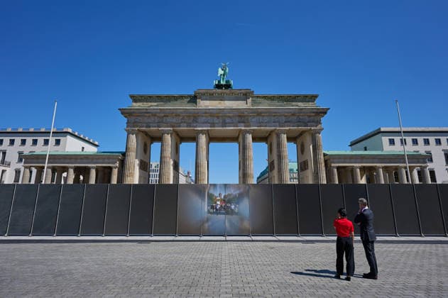 Ein temporaerer Gedenkort am Brandenburger Tor soll zum 65. Jahrestag des Mauerbaus an die deutsche Teilung erinnern (Foto vom 12.08.2026, im Bild: Menschen vor und hinter der Installation). Die rund drei Meter hohe und 30 Meter lange Installation des Kuenstlers Hubertus Hamm auf dem Platz des 18. Maerz soll an die einstigen Grenzanlagen erinnern. Je nach Perspektive wirkt die Wand aus Aluminium lichtundurchlaessig oder transparent. (Siehe epd-Meldung vom 12.08.2026) EDITORIAL USE ONLY *** A temporary memorial site at the Brandenburg Gate is intended to commemorate the division of Germany on the 65th anniversary of the construction of the Berlin Wall. Photo taken on August 12, 2026, showing people in front of and behind the installation. Th Copyright: epd-bild ChristianxDitsch D26D0812MauerbauInstallation141700