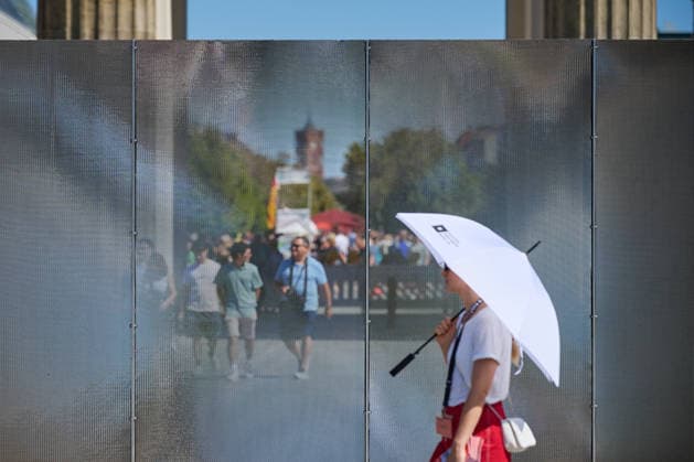 Ein temporaerer Gedenkort am Brandenburger Tor soll zum 65. Jahrestag des Mauerbaus an die deutsche Teilung erinnern (Foto vom 12.08.2026, im Bild: Menschen vor und hinter der Installation). Die rund drei Meter hohe und 30 Meter lange Installation des Kuenstlers Hubertus Hamm auf dem Platz des 18. Maerz soll an die einstigen Grenzanlagen erinnern. Je nach Perspektive wirkt die Wand aus Aluminium lichtundurchlaessig oder transparent. (Siehe epd-Meldung vom 12.08.2026) EDITORIAL USE ONLY *** A temporary memorial site at the Brandenburg Gate is intended to commemorate the division of Germany on the 65th anniversary of the construction of the Berlin Wall. Photo taken on August 12, 2026, showing people in front of and behind the installation. Th Copyright: epd-bild ChristianxDitsch D26D0812MauerbauInstallation141834