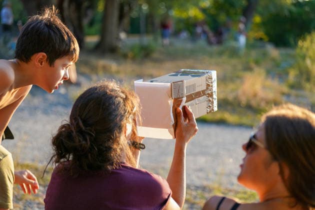 Altenrhein, Bodensee, Schweiz: Familie beobachtet eine Sonnenfinsternis mit selbstgebauter Lochkamera aus Karton zur indirekten Sonnenbeobachtung. Kinder und Erwachsene verfolgen das astronomische Ereignis im Freien. Sonnenfinsternis, partielle Sonnenfinsternis, Sofi, Astronomie, Sonne, Lochkamera, Projektionsmethode, Augenschutz, Kinder, Familie, Naturphänomen, Wissenschaft, Altenrhein, Bodensee, St. Gallen, Schweiz. *** Altenrhein, Lake Constance, Switzerland: A family observes a solar eclipse using a homemade pinhole camera made of cardboard for indirect solar observation. Children and adults watch the astronomical event outdoors. Solar eclipse, partial solar eclipse, Sofi, astronomy, Sun, pinhole camera, projection method, eye prot Copyright: xJOERANxSTEINSIEKx