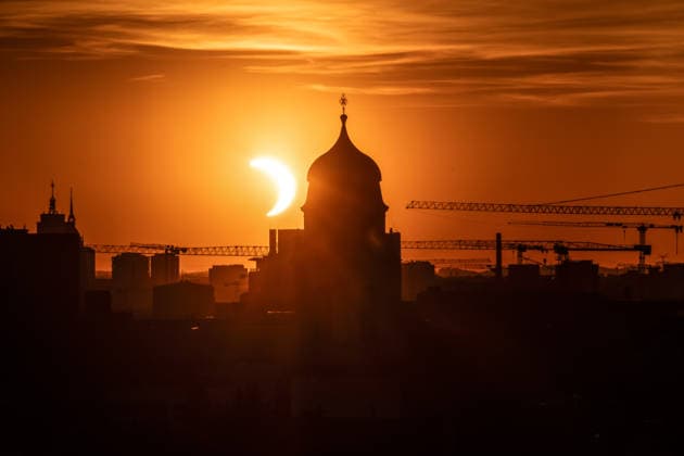Partielle Sonnenfinsternis kurz nach ihrem Höhepunkt um 20:29 Uhr, Sonnensichel versinkt hinter dem Horizont neben dem Kirchturm von St. Wolfgang, Stadtteil Haidhausen, München, 12. August 2026 Deutschland, München, 12. August 2026, partielle Sonnenfinsternis kurz nach ihrem Höhepunkt um 20:29 Uhr, Sonnensichel versinkt neben dem markanten Zwiebelturm von St. Wolfgang in Haidhausen, der Mond schiebt sich vor die tiefstehende Sonne und deckt sie zu 89 Prozent ab, Sonnensichel kurz vor dem Sonnenuntergang um 20:32 Uhr, der Münchner Abendhimmel leuchtet in Orange, Blick von einem Hochhaus an der Rosenheimer Straße stadteinwärts, die katholische Pfarrkirche St. Wolfgang wurde 1920 eingeweiht, Astronomie, Sommer, Bayern, bayerisch, *** Pa