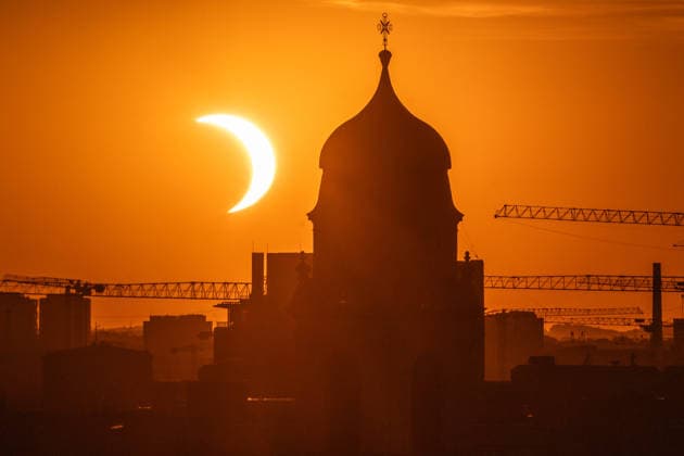 Partielle Sonnenfinsternis 10 Minuten nach ihrem Höhepunkt um 20:25 Uhr, Sonnensichel versinkt hinter dem Horizont neben dem Kirchturm von St. Wolfgang, Stadtteil Haidhausen, München, 12. August 2026 Deutschland, München, 12. August 2026, partielle Sonnenfinsternis kurz nach ihrem Höhepunkt um 20:25 Uhr, Sonnensichel versinkt neben dem markanten Zwiebelturm von St. Wolfgang in Haidhausen, der Mond schiebt sich vor die tiefstehende Sonne und deckt sie zu 89 Prozent ab, Sonnensichel kurz vor dem Sonnenuntergang um 20:32 Uhr, der Münchner Abendhimmel leuchtet in Orange, Blick von einem Hochhaus an der Rosenheimer Straße stadteinwärts, die katholische Pfarrkirche St. Wolfgang wurde 1920 eingeweiht, Astronomie, Sommer, Bayern, bayerisch,