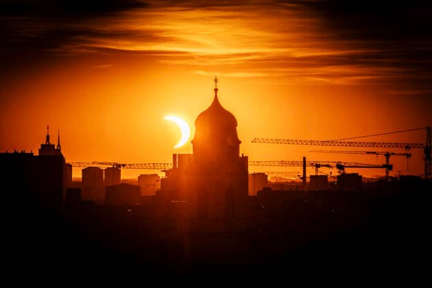 Partielle Sonnenfinsternis um 20:25 Uhr, kurz nach ihrem Höhepunkt, die Sonnensichel nähert sich dem Horizont neben dem Kirchturm von St. Wolfgang, der Münchner Abendimmel leuchtet in Orange, München, 12. August 2026 Deutschland, München, 12. August 2026, Partielle Sonnenfinsternis um 20:25 Uhr, kurz nach ihrem Höhepunkt, die Sonnensichel nähert sich dem Horizont, neben dem dem markanten Zwiebelturm von St. Wolfgang in Haidhausen, der Mond schiebt sich vor die tiefstehende Sonne und deckt sie zu 89 Prozent ab, Sonnensichel kurz vor dem Sonnenuntergang um 20:32 Uhr, der Münchner Abendhimmel leuchtet in Orange, Blick von einem Hochhaus an der Rosenheimer Straße stadteinwärts, die katholische Pfarrkirche St. Wolfgang wurde 1920 ei