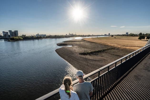 Extremes Niedrigwasser am Rhein, durch Trockenheit freigelegte Uferzone, Blick von der Rheinkniebrücke, Düsseldorf, 13. August 2026 Deutschland, Düsseldorf, 13. August 2026, Niedrigwasser im Rhein, Blick von der Rheinkniebrücke durch Trockenheit freigelegten Uferzonen und die verdorrten Rheinwiesen, weit zurückgewichenes Rheinufer, durch die anhaltende Trockenheit ist der Pegelstand des Rheins auf extrem niedrigen Niveau, die Schifffahrt ist eingeschränkt, zu wenig Regen, schönes Wetter, Hochsommer, Hitzewelle mit Temperaturen bis 33 Grad, im Vordergrund zwei Spaziergänger am Donnerstagabend, Sommer, Nordrhein-Westfalen, NRW, *** Extremely low water levels on the Rhine; riverbanks exposed due to drought; view from the Rheinknie Bri