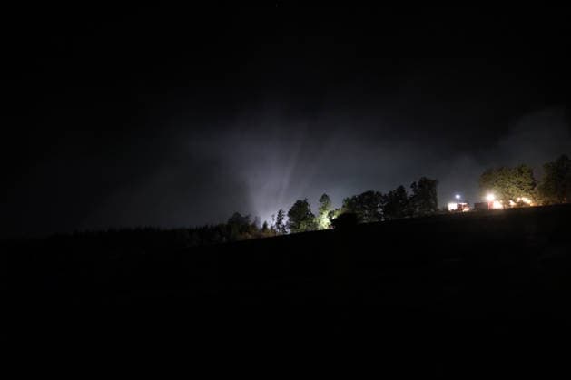 Marsberg, Nordrhein-Westfalen, Deutschland, Europa: Weitwinkelaufnahme eines nächtlichen Waldbrandeinsatzes nahe der Diemeltalsperre. Dichter Rauch steigt über dem Wald auf und wird von Scheinwerfern und Einsatzbeleuchtung angestrahlt. Feuerwehrfahrzeuge und Einsatzkräfte setzen die Löscharbeiten entlang des Waldrandes während der Nacht fort. *** Marsberg, North Rhine-Westphalia, Germany, Europe: A wide-angle shot of a nighttime forest fire operation near the Diemel Dam. Thick smoke rises above the forest and is illuminated by spotlights and emergency lights. Fire trucks and emergency personnel continue firefighting operations along the edge of the forest throughout the night. Copyright: xAymanxAlahmedx