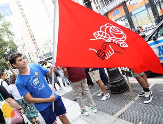 August 13, 2026, New York, New York, USA: A man with a Democratic Socialist of American (DSA) flag joins the Amazon Teamsters and Allies picket outside of City Hall for passage of the Delivery Protection Act. The Delivery Protection Act would require companies like Amazon to hire its workforce directly, essentially making Amazons corrupt third-party Delivery Service Partner model illegal in New York City. New York USA  - ZUMAk03_ 20260813_zaf_k03_068 Copyright: xNancyxKaszermanx