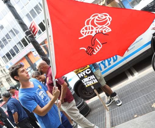 August 13, 2026, New York, New York, USA: A man with a Democratic Socialist of American (DSA) flag joins the Amazon Teamsters and Allies picket outside of City Hall for passage of the Delivery Protection Act. The Delivery Protection Act would require companies like Amazon to hire its workforce directly, essentially making Amazons corrupt third-party Delivery Service Partner model illegal in New York City. New York USA - ZUMAk03_ 20260813_zaf_k03_067 Copyright: xNancyxKaszermanx