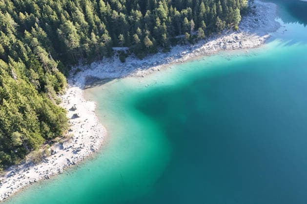 Wetterfeature, Morgenstille am Eibsee: Unterhalb der Zugspitze liegt der See bei Grainau nahe Garmisch-Partenkirchen in den frühen Stunden noch ruhig und nahezu unberührt. Doch an heißen Sommertagen ändert sich das Bild häufig schon ab Mittag. Dann strömen zahlreiche Ausflügler und Urlauber an den durch soziale Medien weltweit bekannt gewordenen Bergsee. Der zunehmende Massentourismus sorgt regelmäßig für einen regelrechten Besucheransturm. Unter dem hohen Verkehrsaufkommen, zugeparkten Straßen und dem großen Andrang leiden zunehmend auch die Anwohner in Grainau und rund um den Eibsee. (Aufnahme mit einer Drohne) Grainau Bayern Deutschland Grainau *** Weather Feature, Morning Stillness at Eibsee. Nestled below the Zugspitze near Copyright: x xonw-imagesx xMariusxBullingx