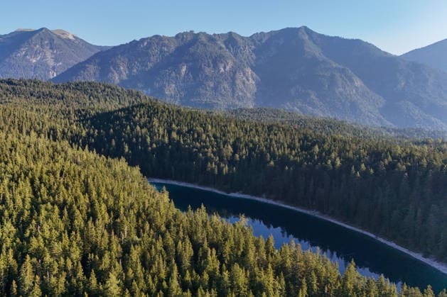Wetterfeature, Morgenstille am Eibsee: Unterhalb der Zugspitze liegt der See bei Grainau nahe Garmisch-Partenkirchen in den frühen Stunden noch ruhig und nahezu unberührt. Doch an heißen Sommertagen ändert sich das Bild häufig schon ab Mittag. Dann strömen zahlreiche Ausflügler und Urlauber an den durch soziale Medien weltweit bekannt gewordenen Bergsee. Der zunehmende Massentourismus sorgt regelmäßig für einen regelrechten Besucheransturm. Unter dem hohen Verkehrsaufkommen, zugeparkten Straßen und dem großen Andrang leiden zunehmend auch die Anwohner in Grainau und rund um den Eibsee. (Aufnahme mit einer Drohne) Grainau Bayern Deutschland Grainau *** Weather Feature, Morning Stillness at Eibsee. Nestled below the Zugspitze near Copyright: x xonw-imagesx xMariusxBullingx