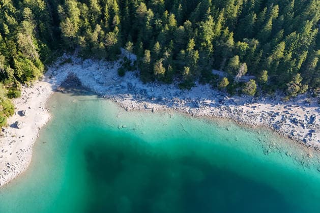 Wetterfeature, Morgenstille am Eibsee: Unterhalb der Zugspitze liegt der See bei Grainau nahe Garmisch-Partenkirchen in den frühen Stunden noch ruhig und nahezu unberührt. Doch an heißen Sommertagen ändert sich das Bild häufig schon ab Mittag. Dann strömen zahlreiche Ausflügler und Urlauber an den durch soziale Medien weltweit bekannt gewordenen Bergsee. Der zunehmende Massentourismus sorgt regelmäßig für einen regelrechten Besucheransturm. Unter dem hohen Verkehrsaufkommen, zugeparkten Straßen und dem großen Andrang leiden zunehmend auch die Anwohner in Grainau und rund um den Eibsee. (Aufnahme mit einer Drohne) Grainau Bayern Deutschland Grainau *** Weather Feature, Morning Stillness at Eibsee. Nestled below the Zugspitze near Copyright: x xonw-imagesx xMariusxBullingx