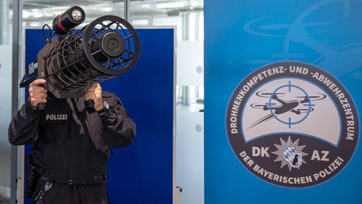Drohnendetektion und -abwehr der Bayerischen Polizei, Flughafen Nürnberg, 14.08.2026 Ein Polizeibeamter demonstriert das tragbare, schultergestützte Störsender-System Counter UAV Jammer HP 47+ PRO V7 zur Drohnendetektion und -abwehr. Das Gerät wird wie ein Rohrsystem auf der Schulter gehalten und zielgerichtet ausgerichtet.. Im Hintergrund informiert ein Banner über die Möglichkeiten zur Drohnendetektion und -abwehr sowie den geplanten Ausbau technischer und personeller Ressourcen der Grenzpolizeiinspektion. Nürnberg Flughafen Bayern Deutschland *** Drone Detection and Defense by the Bavarian Police, Nuremberg Airport, August 14, 2026 A police officer demonstrates the portable, shoulder-mounted jamming system, the Counter UAV Jammer 20260814-286A5445-M4000