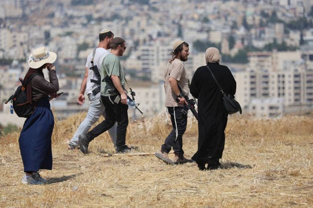 Activists Remove Flags From Beit Sahour Armed men walk past two women in an open field in Beit Sahour, east of Bethlehem in the occupied West Bank, on August 14, 2026. The activists said settlers had placed the symbols on the house after October 7, 2023, in what they described as an attempt to seize control of the property, and that settlers opened fire toward them as the items were removed, with no injuries reported. Bethlehem West Bank Palestinian Territories Copyright: xMosabxShawerx