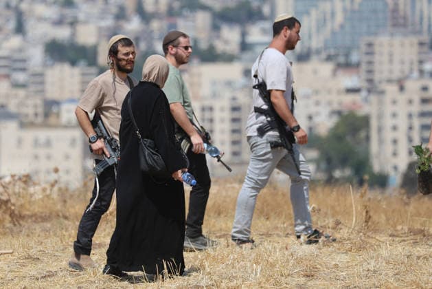 Activists Remove Flags From Beit Sahour Armed men walk across open ground near a woman in Beit Sahour, east of Bethlehem in the occupied West Bank, on August 14, 2026. The activists said settlers had placed the symbols on the house after October 7, 2023, in what they described as an attempt to seize control of the property, and that settlers opened fire toward them as the items were removed, with no injuries reported. Bethlehem West Bank Palestinian Territories Copyright: xMosabxShawerx