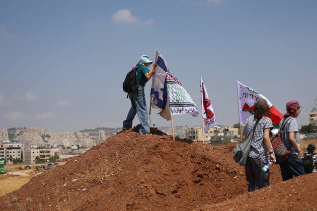 Activists Remove Flags From Beit Sahour Activists stand on and around a mound of earth with several flags during the action in Beit Sahour, east of Bethlehem in the occupied West Bank, on August 14, 2026. The activists said settlers had placed the symbols on the house after October 7, 2023, in what they described as an attempt to seize control of the property, and that settlers opened fire toward them as the items were removed, with no injuries reported. Bethlehem West Bank Palestinian Territories Copyright: xMosabxShawerx