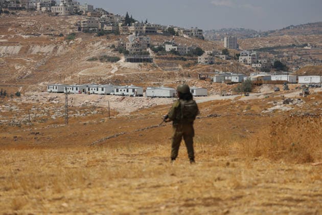 Activists Remove Flags From Beit Sahour An armed uniformed man stands in an open field overlooking nearby hills in Beit Sahour, east of Bethlehem in the occupied West Bank, on August 14, 2026. The activists said settlers had placed the symbols on the house after October 7, 2023, in what they described as an attempt to seize control of the property, and that settlers opened fire toward them as the items were removed, with no injuries reported. Bethlehem West Bank Palestinian Territories Copyright: xMosabxShawerx