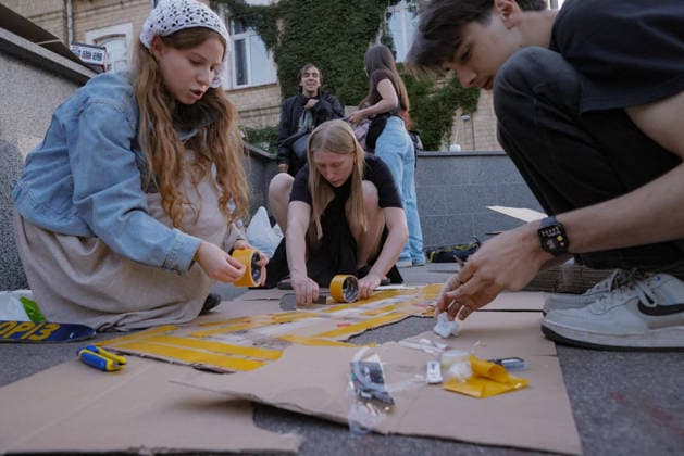 Kharkiv Protesters Demand Reinstatement of Defence Minister Fedorov - Ukraine Activists kneel on the ground and use yellow packing tape to assemble cardboard protest signs at a rally on Freedom Square in Kharkiv, Ukraine, on August 14, 2026. Demonstrators gathered to demand the reinstatement of Mykhailo Fedorov as Minister of Defence, part of nationwide protests running since July 24. Photo by Yevhen Titov ABACAPRESS.COM Kharkiv Kharkiv Oblast Ukraine  Copyright: xTitovxYevhen ABACAx