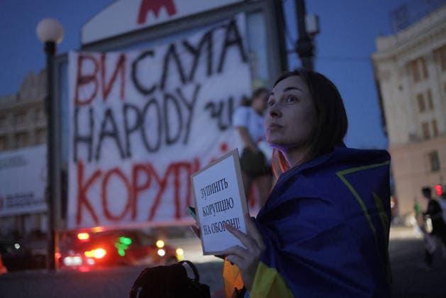 Kharkiv Protesters Demand Reinstatement of Defence Minister Fedorov - Ukraine A woman draped in a Ukrainian flag holds a sign reading ???????? ???????? ?? ???????! ( Stop corruption in defence! ) at a protest on Freedom Square in Kharkiv, Ukraine, on August 14, 2026. A large banner behind her reads ?? ????? ?????? ???????? ( You are a servant of the people of corruption ), as demonstrators gathered to demand the reinstatement of dismissed Defence Minister Mykhailo Fedorov on the 29th day of nationwide protests. Photo by Yevhen Titov ABACAPRESS.COM Kharkiv Kharkiv Oblast Ukraine  Copyright: xTitovxYevhen ABACAx