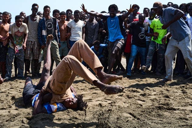 (260815) -- CEUTA, Aug. 15, 2026 -- Irregular migrants take part in a freestyle wrestling match on Trampolin Beach in Ceuta, Spain, Aug. 15, 2026. More than 72,000 migrants crossed irregularly into Ceuta from neighboring Morocco on July 30 and 31, according to the Spanish government. Most returned to Morocco later, while thousands remain in the enclave.Security was also tightened along the border ahead of Saturday after calls for another mass crossing circulated on social media. Moroccan security forces intercepted hundreds of migrants attempting to reach the border area, while Ceuta reported no influx on a scale comparable to that seen in late July. ) SPAIN-CEUTA-VIEW MengxDingbo 