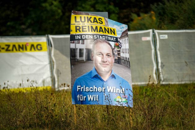 Schweiz: Politik, Wahlkampf in Wil (SG); Wahlplakat der Schweizerischen Volkspartei (SVP) mit dem Kandidaten Lukas Reimann und der Aufschrift Lukas Reimann in den Stadtrat Frischer Wind für Wil. Das Plakat steht am Strassenrand auf einer Grünfläche. Symbolbild für Kommunalpolitik, Wahlen, SVP, Stadt Wil und politischen Wahlkampf. *** Swiss Politics, Election Campaign in Wil, SG: Election poster for the Swiss People s Party (SVP) featuring candidate Lukas Reimann and the slogan Lukas Reimann for City Council—A Breath of Fresh Air for Wil. The poster is displayed on the side of the road in a green space. Symbolic image representing local politics, elections, SVP, the city of Wil, and political campaigns Copyright: xJOERANxSTEINSIEKx