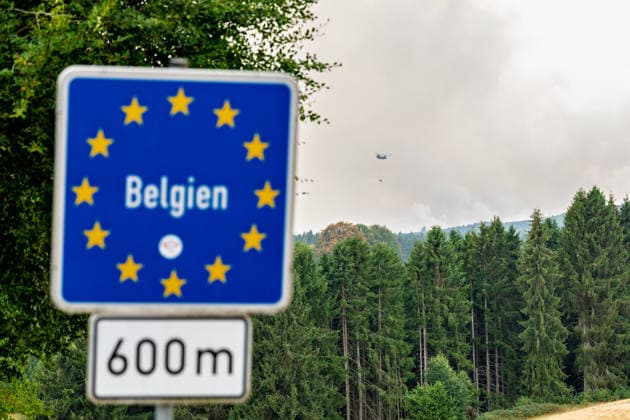 News Bilder des Tages Waldbrand im Hohen Venn Blick von der deutsch-belgischen Grenze bei Kalterherberg - 15.08.26 Blick von Kalterherberg (Gemeinde Monschau) auf den Großbrand im Hohen Venn nahe der deutsch-belgischen Grenze. Im Vordergrund ein blaues Grenzschild im Hintergrund Rauchsäulen des Feuers und ein Löschhubschrauber mit Wasserbehälter im Anflug. Insgesamt zwei Löschhubschrauber sind im Einsatz und werfen jeweils rund 3.000 Liter Wasser ab. Der Hochmoorbrand hat bereits rund 2.000 Hektar Wald- und Moorgebiet erfasst, die tiefen Torfschichten begünstigen einen langanhaltenden Schwelbrand. Auf belgischer Seite laufen bereits Evakuierungen, für Teile Monschaus wird eine mögliche Räumung vorbereitet. Monschau Kalterherberg Nordrhein-Westfalen Copyright: xMarcxJohnx
