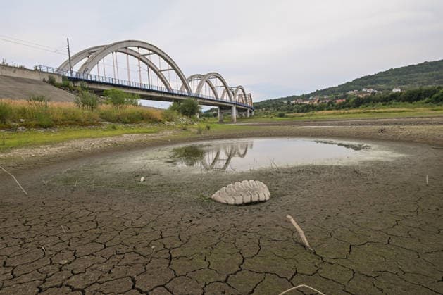 Historic summer heatwave drains southern Poland waterways ZEMBRZYCE, POLAND - AUGUST 17: A large tractor tire stands half-buried in an expanse of deeply cracked, parched earth near a shrinking pool of stagnant water, with an arched railway bridge in the background in Zembrzyce, southern Poland, on August 17, 2026. A record-breaking summer heatwave and acute lack of rainfall have caused the Skawa River water levels to plummet by over a meter, exposing dumped waste and long-hidden artifacts across the parched basin. The critical hydrological drought has forced regional authorities to enforce emergency water restrictions across the Malopolska province. Artur Widak Anadolu Zembrzyce Poland. Editorial use only. Please get in touch for any othe  Copyright: x2026xAnadoluxArturxWidakx