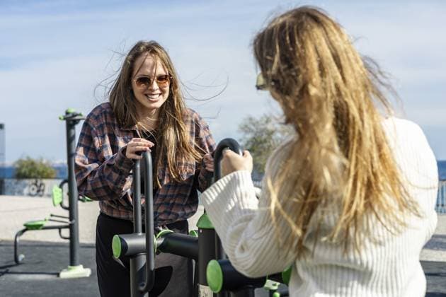 Zwei junge kaukasische Frauen mit langen Haaren trainieren draußen in einem Fitnesspark. Eine Frau trägt eine Sonnenbrille und ein kariertes Hemd, während die andere einen weißen Pullover trägt Two young Caucasian women with long hair exercise outdoors at a fitness park. One woman wears sunglasses and a plaid shirt, while the other wears a white sweater Copyright: imageBROKER AlinaxKandybka ibxayk18797357.jpg ,model released, Symbolfoto ,property released