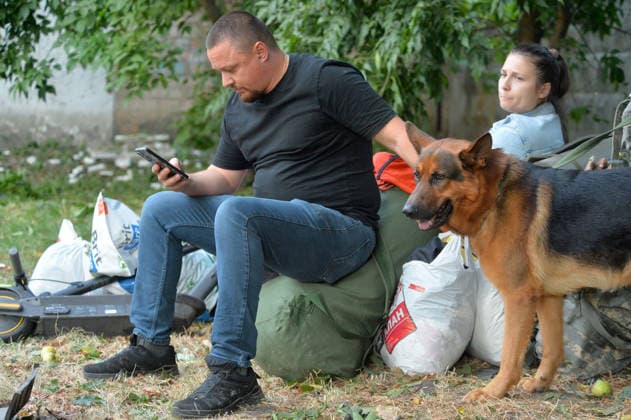 A man looking at a smartphone pets a German Shepherd dog as people stay outside an apartment block in the Solomianskyi district after a Russian missile attack, Kyiv, Ukraine, August 20, 2026. High-rise residential buildings, a children’s hospital, a school, utility and warehouse facilities, garages, and cars were damaged in the district as a result of Russia’s overnight large-scale combined strike on the capital. Power grid infrastructure was also affected, causing an outage. In Kyiv, the attack claimed the lives of at least 13 people, including two children. The Russian military targeted the city with ballistic missiles, Kalibr cruise missiles, Kh-101s, and Zircon hypersonic cruise missiles. (Photo by Oleksandr Klymenko Ukrinform) Aftermat  Copyright: xOleksandrxKlymenkox