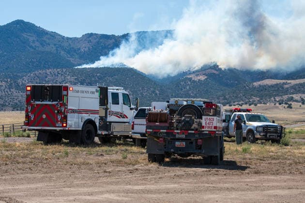 August 23, 2026, Elberta, Utah, USA: A plume of thick smoke rises into the sky above a mountain ridge as the Big Mountain Fire burns southwest of Elberta, Utah, United States, on August 23, 2026. A line of emergency response vehicles can be seen staged along a dirt road below the active wildland blaze. Elberta USA  - ZUMAm292 20260823_znp_m292_001 Copyright: xCharlesxMcClintockxWilsonx