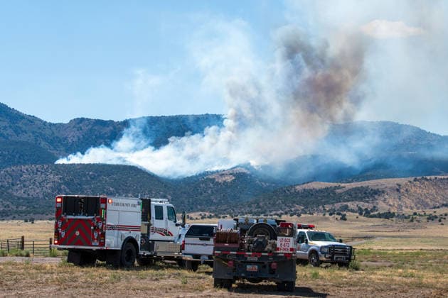 August 23, 2026, Elberta, Utah, USA: A plume of thick smoke rises into the sky above a mountain ridge as the Big Mountain Fire burns southwest of Elberta, Utah, United States, on August 23, 2026. A line of emergency response vehicles can be seen staged along a dirt road below the active wildland blaze. Elberta USA  - ZUMAm292 20260823_znp_m292_002 Copyright: xCharlesxMcClintockxWilsonx