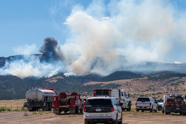 August 23, 2026, Elberta, Utah, USA: A plume of thick smoke rises into the sky above a mountain ridge as the Big Mountain Fire burns southwest of Elberta, Utah, United States, on August 23, 2026. A line of emergency response vehicles can be seen staged along a dirt road below the active wildland blaze. Elberta USA  - ZUMAm292 20260823_znp_m292_004 Copyright: xCharlesxMcClintockxWilsonx