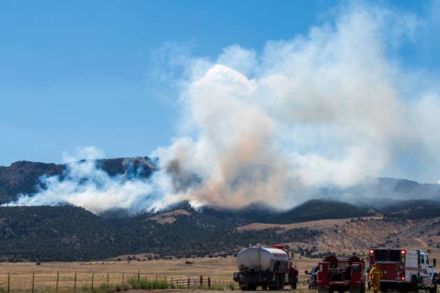 August 23, 2026, Elberta, Utah, USA: A plume of thick smoke rises into the sky above a mountain ridge as the Big Mountain Fire burns southwest of Elberta, Utah, United States, on August 23, 2026. A line of emergency response vehicles can be seen staged along a dirt road below the active wildland blaze. Elberta USA  - ZUMAm292 20260823_znp_m292_005 Copyright: xCharlesxMcClintockxWilsonx