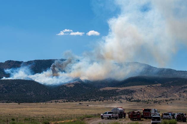 August 23, 2026, Elberta, Utah, USA: A plume of thick smoke rises into the sky above a mountain ridge as the Big Mountain Fire burns southwest of Elberta, Utah, United States, on August 23, 2026. A line of emergency response vehicles can be seen staged along a dirt road below the active wildland blaze. Elberta USA  - ZUMAm292 20260823_znp_m292_007 Copyright: xCharlesxMcClintockxWilsonx