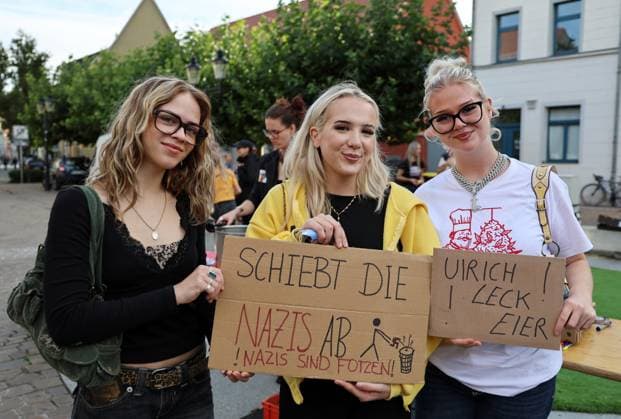 Wahlkampf der AfD zur Landtagswahl in Sachsen-Anhalt 24.08.2026, Naumburg, Wahlkampf der AfD auf dem Naumburger Marktplatz, am 06.09.2026 wird der neue Landtag in Sachsen-Anhalt gewaehlt im Bild: Gegenveranstaltung auf dem Holzmarkt - junge Frauen halten Schilder mit der Aufschrift Schiebt die Nazis ab! Nazis sind Fotzen! und Ulrich Leck Eier - gemeint ist Urlich Siegmund *** AfD campaign for the state election in Saxony-Anhalt on August 24, 2026, Naumburg; AfD campaign rally on Naumburg’s market square, On September 6, 2026, the new state parliament in Saxony-Anhalt will be elected. Pictured: a counter-demonstration at the Holzmarkt, where young women are holding signs reading Kick out the Nazis, Nazis are cunts, and Ulrich Leck E