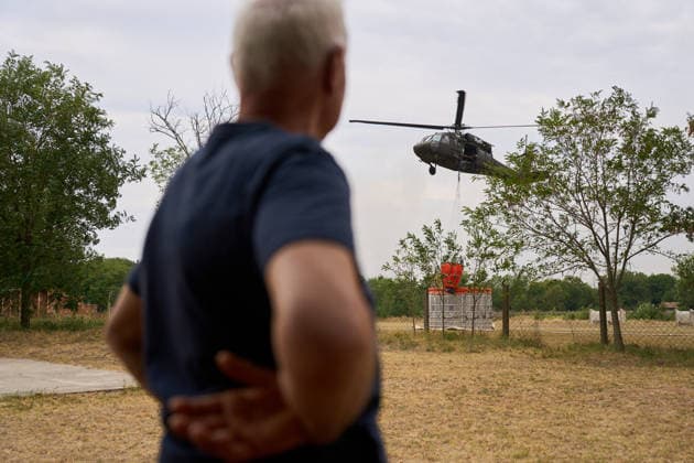 August 25, 2026, Susara, Vojvodina, Serbia: 2026825, Susara, Serbia - Two Sikorsky UH-60 Black Hawk helicopters are deployed to the village of Susara to help battle the severe wildfires devastating the Deliblato Sands (Deliblatska Pescara) Special Nature Reserve, refilling their buckets from a large portable water tank placed on a local football pitch. A local resident watches a Slovak helicopter scooping water. Susara Serbia  - ZUMAd223 20260825_zip_d223_002 Copyright: xMarkoxDimicx