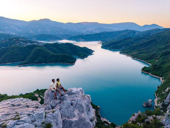 Atemberaubender Blick auf den Bovilla-Stausee bei Sonnenuntergang in Albanien Two friends admire the breathtaking scenery from a rocky outcrop overlooking Bovilla Reservoir in Albania, where lush green hills meet tranquil waters at sunset, creating a serene atmosphere. (License=RF) ,model released, Symbolfoto Copyright: xZoonar.com FokkexBaarssenx 25494884 ,model released, Symbolfoto ,property released