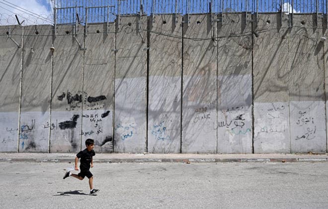 A Palestinian boy runs beside the Israeli separation wall that cuts through Beit Hanina in East Jerusalem on Sunday, August 30, 2026. Thousands of Palestinian residents of East Jerusalem are forced to go through time consuming checkpoints to reach their schools, jobs, hospitals and visit family because of the separation barrier.  JER2026083009 DEBBIExHILL