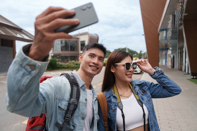 Ein fröhliches asiatisches Touristenpaar macht während einer Stadtrundfahrt ein Selfie mit dem Smartphone Young man and woman on vacation taking a self portrait picture with a mobile phone while exploring an outdoor location. (License=RF) ,model released, Symbolfoto Copyright: xZoonar.com WORAWEExMEEPIANx 25523042 ,model released, Symbolfoto ,property released