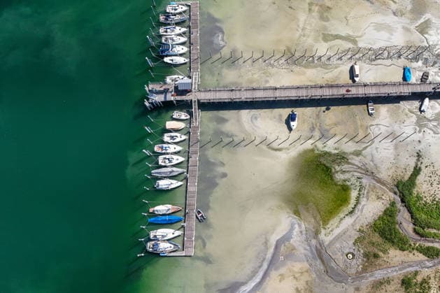 Wetterfeature, Bei sonnigem Spätsommerwetter am Bodensee liegen einige Boote aufgrund des niedrigen Wasserstands auf dem Trockenen. Gleichzeitig zeigt sich der Bodensee von seiner malerischen Seite das Wasser schimmert bei strahlendem Sonnenschein grünlich-blau, während sich die Uferlandschaft unter nahezu wolkenlosem Himmel präsentiert. (Aufnahme mit einer Drohne) Moos Baden-Württemberg Deutschland Moos