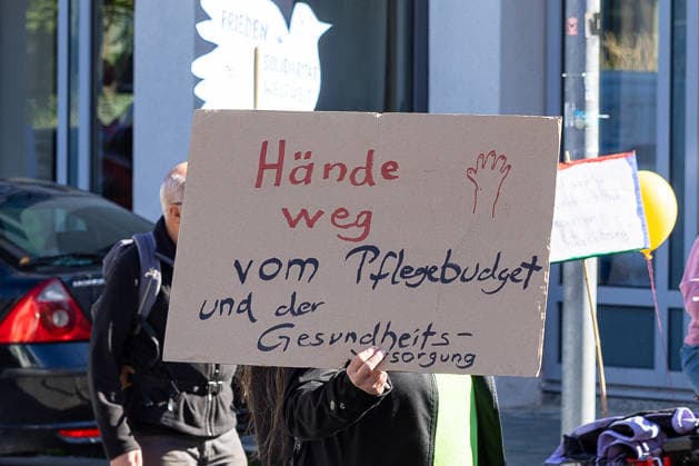 UNKÜRZBAR - Protest gegen Angriffe auf Arbeitnehmer*innenrechte und soziale Infrastruktur, Nürnberg, 26.09.2026 Eine Demonstrantin hält ein Schild mit der Aufschrift Hände weg vom Pflegebudget und der Gesundheitsversorgung in die Höhe. Im Hintergrund sind weitere Protestschilder mit Friedenssymbolen zu sehen. Nürnberg Bayern Deutschland