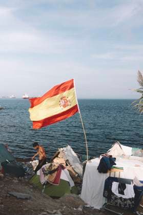 September 26, 2026, Ceuta, Ceuta, Spain: A Spanish flag flies over makeshift shelters built by migrants on the rocky shore of Ceuta, as a man walks between them. Thousands of migrants, most of them young Moroccan men, have been living in makeshift settlements in the Spanish North African enclave of Ceuta since a mass arrival at the end of July 2026 set off a migration and political crisis. Ceuta Spain - ZUMAs392 20260926_zip_s392_008 Copyright: xFabianxSuspensivox