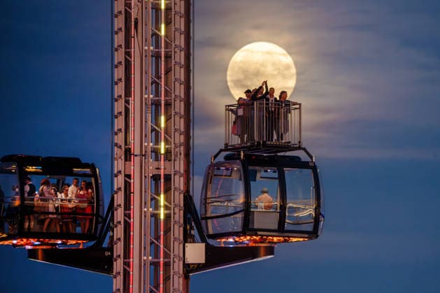 Der Vollmond, auch Erntemond genannt, leuchtet hinter dem SkyLift auf dem Oktoberfest, Wiesnbesucher in den Gondeln und auf der Freifläche machen Fotos mit ihren Smartphones, München, 26. September 2026 Deutschland, München, 26. September 2026, der Vollmond, auch Erntemond genannt, leuchtet hinter dem SkyLift auf dem Oktoberfest, Wiesnbesucher in den Gondeln und auf der Freifläche machen Fotos mit ihren Smartphones, Theresienwies, fast wolkenfreier Abendhimmel, um 19:25 Uhr, Bayern