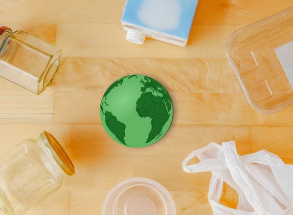 Recycling-Konzept mit einem grünen Erdball, umgeben von Gläsern, einer Plastiktüte, Plastikbehältern und einem Milchkarton auf einem Holztisch, Draufsicht, Nachhaltigkeit und Mülltrennung