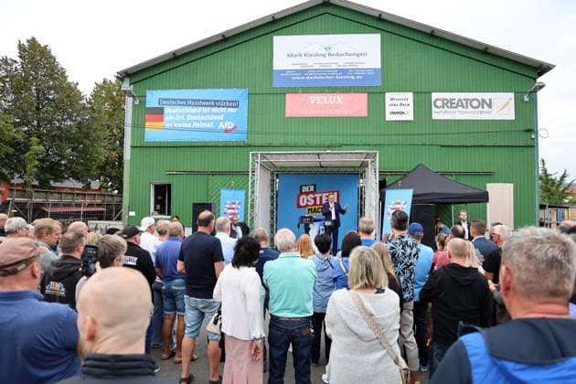 Auf eine Bratwurst mit Haseloff und Chrupalla 01.10.2026, Doellstaedt, Veranstaltung der AfD bei Kiesling Bedachungen, Auf eine Bratwurst mit Landtagsabgeordneten Daniel Haseloff (AfD) und AfD Bundessprecher Tino Chrupalla im Bild: Tino Chrupalla haelt eine Rede auf der Buehne, Besucher der Veranstaltung stehen um die Buehne herum, am Gebaeude der Firma haengt ein grosses Schild mit der Aufschrift Deutsches Handwerk staerken! Deutschland ist nicht nur ein Ort, Deutschland ist meine Heimat