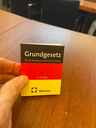 Flensburg, Schleswig-Holstein Lange Nacht der Demokratie im Flensburger Rathaus. Hier: Lektüre des Grundgesetzes in Miniformat. Im Hintergrund der Fotograf und Autor Siegfried Wittenburg. Er berichtet in seinem Vortrag Leben in der Utopie. Der Alltag ohne Freiheit und Demokratie aus seinem Leben in der DDR und verbindet persönliche Erlebnisse mit eigenen Fotografien. Im Mittelpunkt standen Fragen nach Freiheit, Anpassung, Widerstand und persönlicher Verantwortung. Als Zeitzeuge beschreibt er die tiefe Kluft zwischen den glänzenden Zukunftsversprechen einer politischen Führung und der grauen, oft absurden Realität der Bürger. Aufnahme vom 02.10.2026, Flensburg.