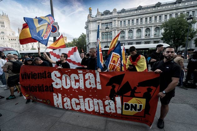 Protest Rally Against the Sol Camp in Madrid: A group of people during a rally against the camp at Puerta del Sol on October 3, 2026, in Madrid, Spain. The Indignados por Espana platform is organizing the protest against the camp at Sol, in support of social and national housing, against mass deportations, and in defense of national sovereignty following the invasion of Ceuta. OCTOBER 3, 2026 NATIONAL CORE HOUSING PROTEST FLAG HOODED PROTESTERS Diego Radamé Madrid, Madrid, Spain  Copyright: xDiegoxRadamÃ sx 7818790