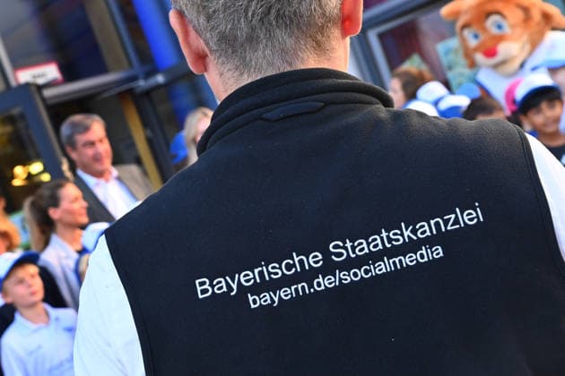 Der Ruecken einer Person mit dem Schriftzug Bayerische Staatskanzlei ,Social Media im Vordergrund eines Schultermins mit Ministerpraesident Markus Soeder. Markus SOEDER (Ministerpraesident Bayern und CSU Vorsitzender) besucht gemeinsam mit Gesundheitsministerin Judith Gerlach und Kultusministerin Anna Stolz am 06.10.2026 die Sport-Grundschule an der Margarethe-Danzi-Straße in Muenchen und informiert sich im Vorfeld des landesweiten Praeventionstages am 12. Oktober über erfolgreiche Praevention und Gesundheitsfoerderung im Schulalltag